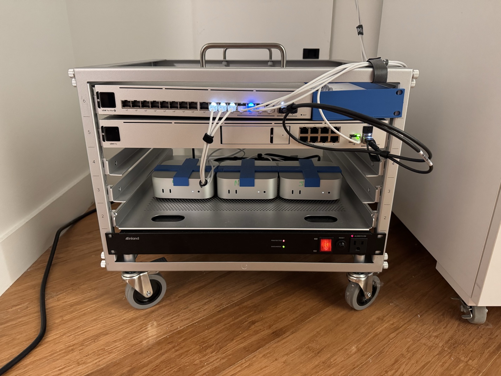 Front view of the rack cart: the three M4 Mac minis side by side in their 3D-printed alignment racks beneath the UniFi gear