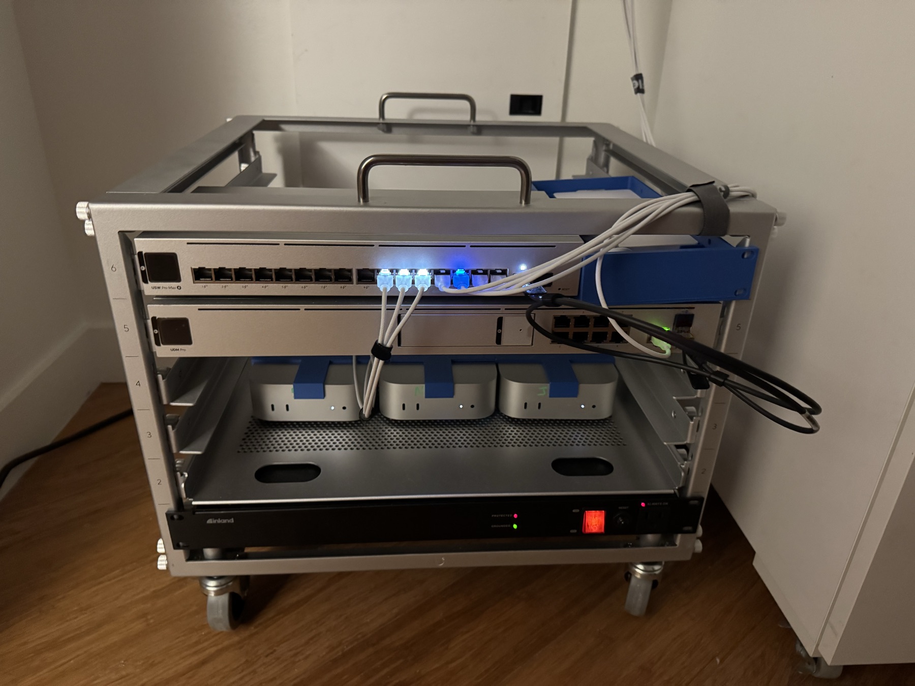 The homelab rack: a UniFi switch and gateway glowing above three M4 Mac minis seated in blue 3D-printed alignment racks